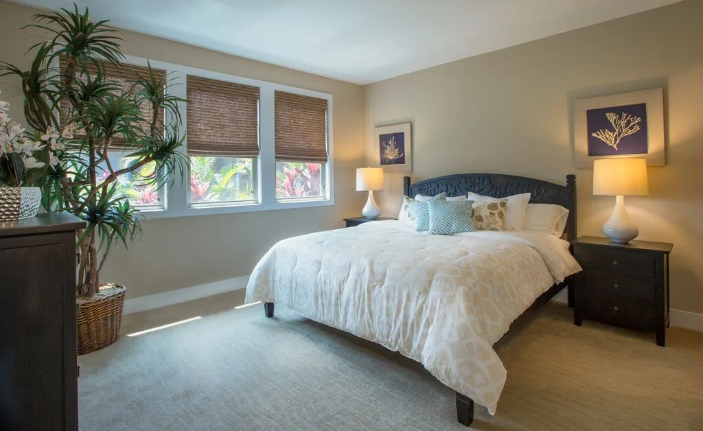 A bedroom with a bed, bedside tables, and windows with blinds.