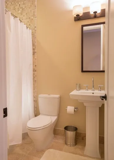 A bathroom with a toilet, pedestal sink, and shower curtain.