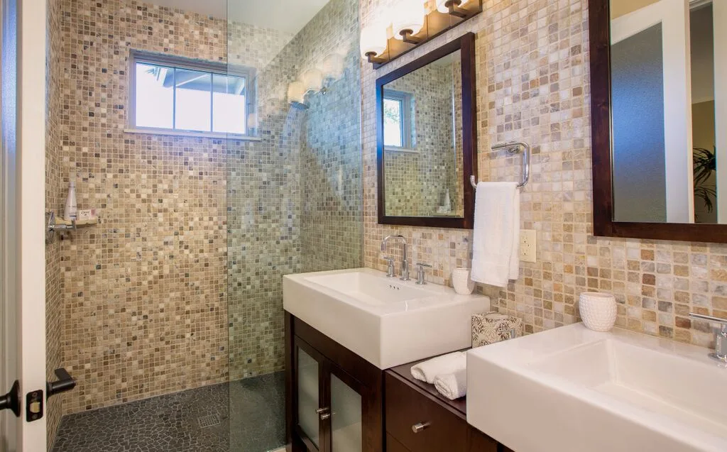 A tiled bathroom with a glass shower, two sinks, and wall mirrors.