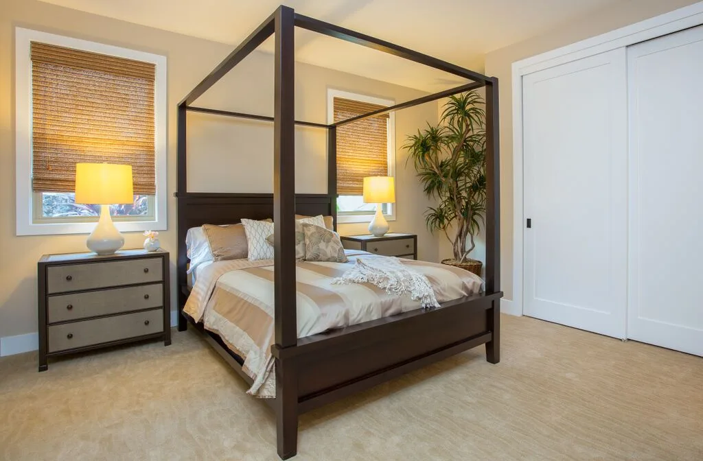 A bedroom with a four-poster bed, bedside tables, and a potted plant.