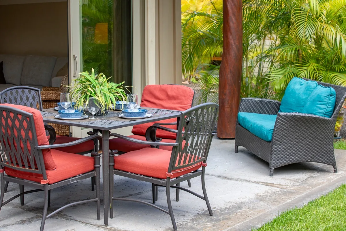 An outdoor patio dining area with cushioned seating and tropical plants.