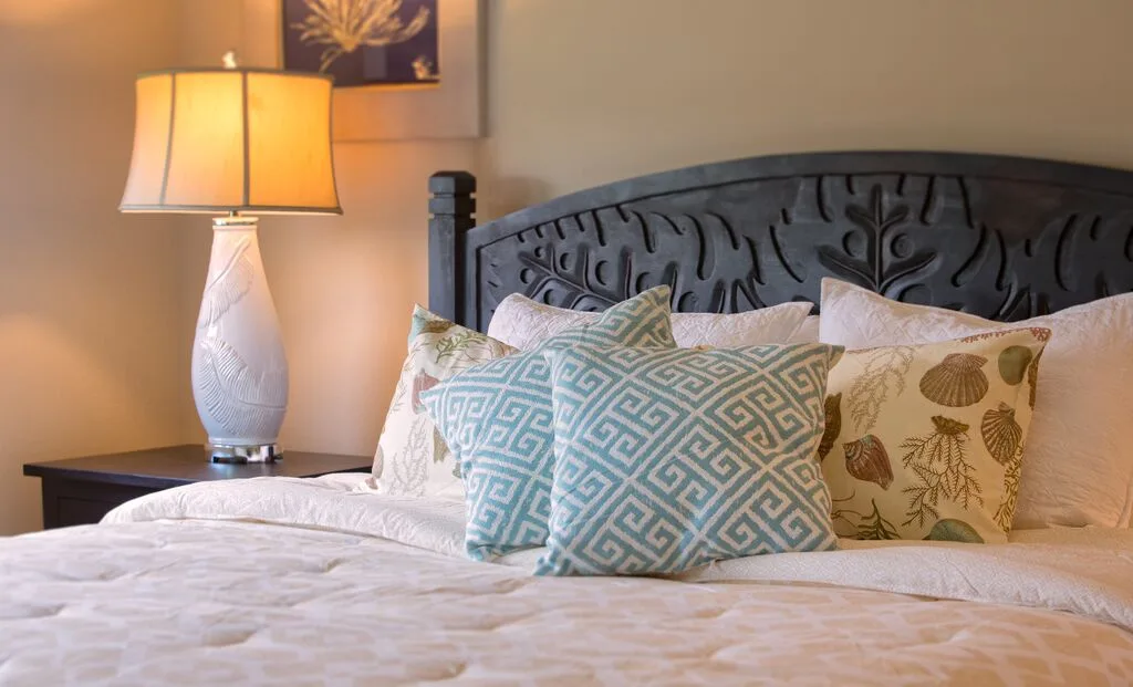 A bedroom with a bed, patterned pillows, and a lit bedside lamp.