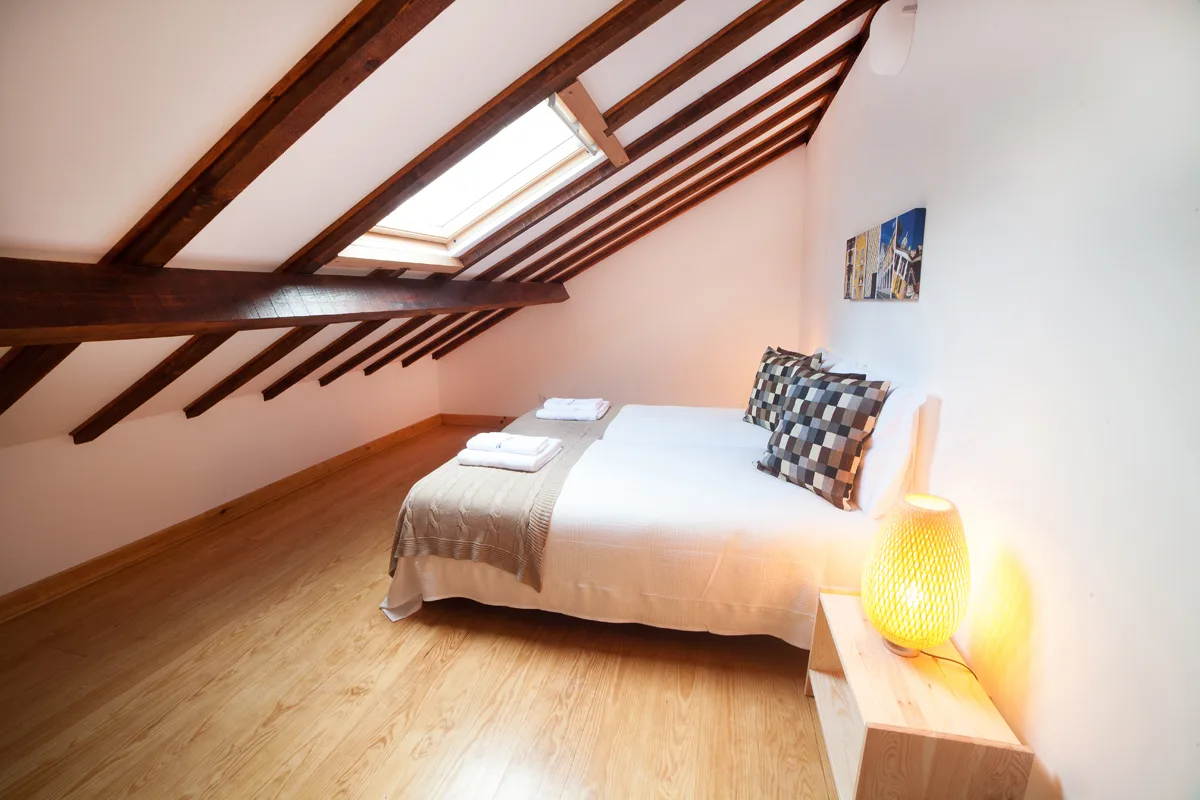 A bedroom with a bed beneath a sloped timber-beamed ceiling.