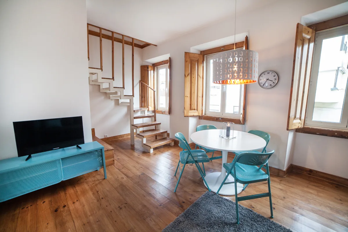 A dining area with a round table and turquoise chairs sits beside a television.