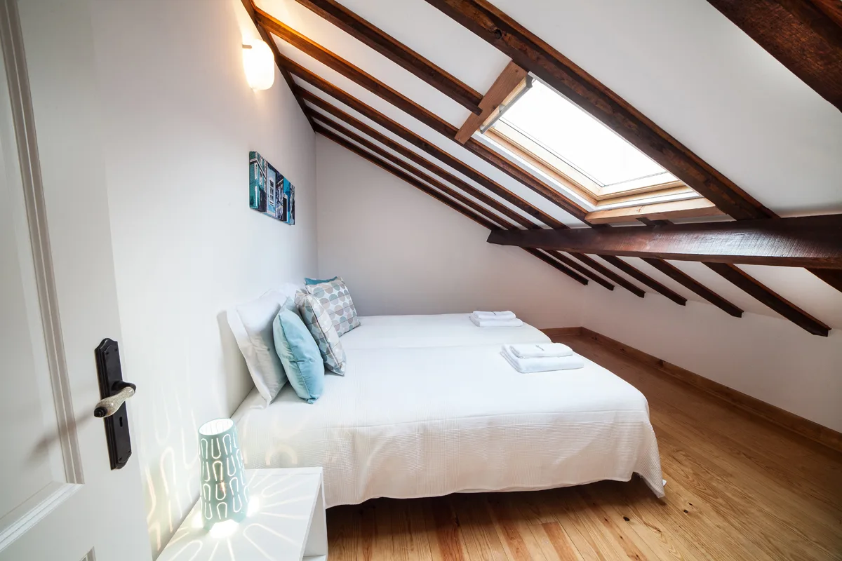 A bedroom with a bed beneath a sloped ceiling and skylight.