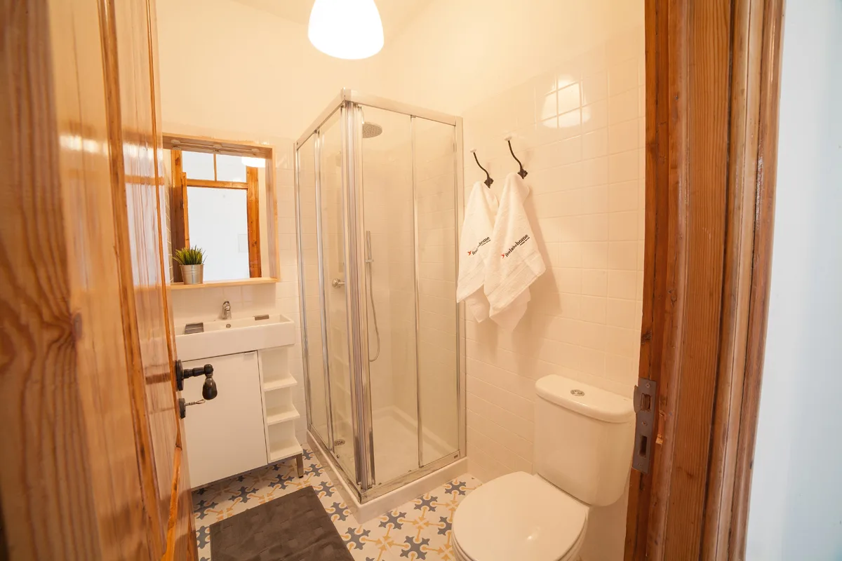 A bathroom with a glass shower, sink, and patterned floor tiles.