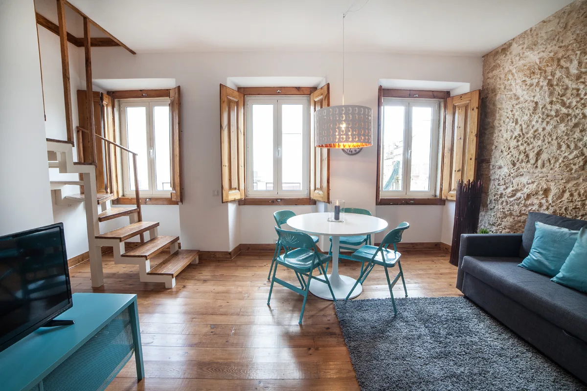A living and dining area with a round table, seating, and three windows.