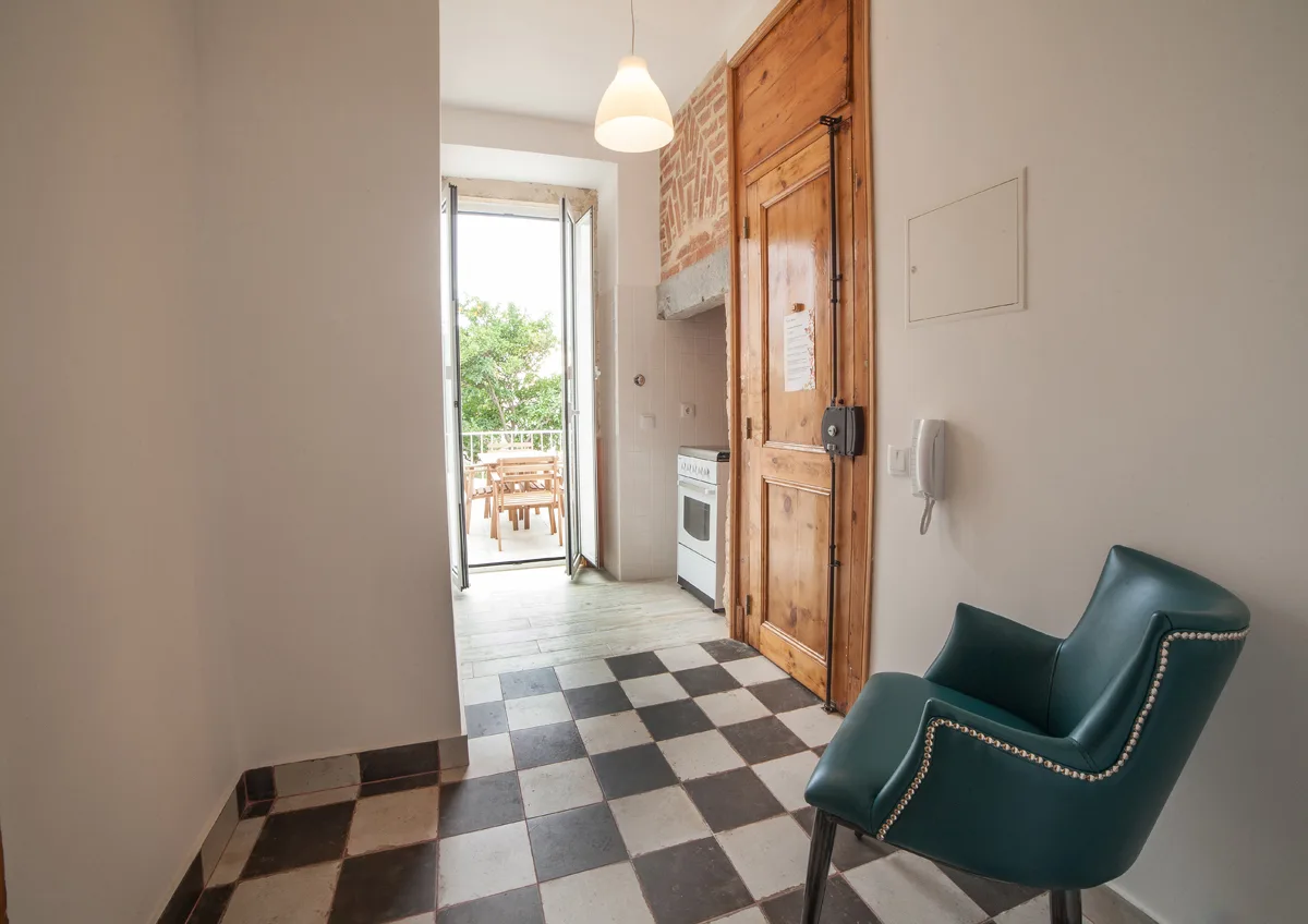 A tiled apartment entryway with a wooden door and a chair.