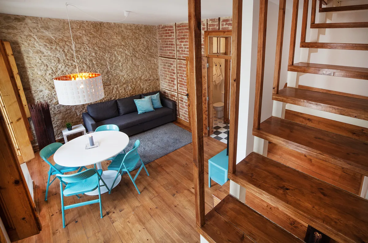 A living room with a dark sofa, white table, and wooden staircase.