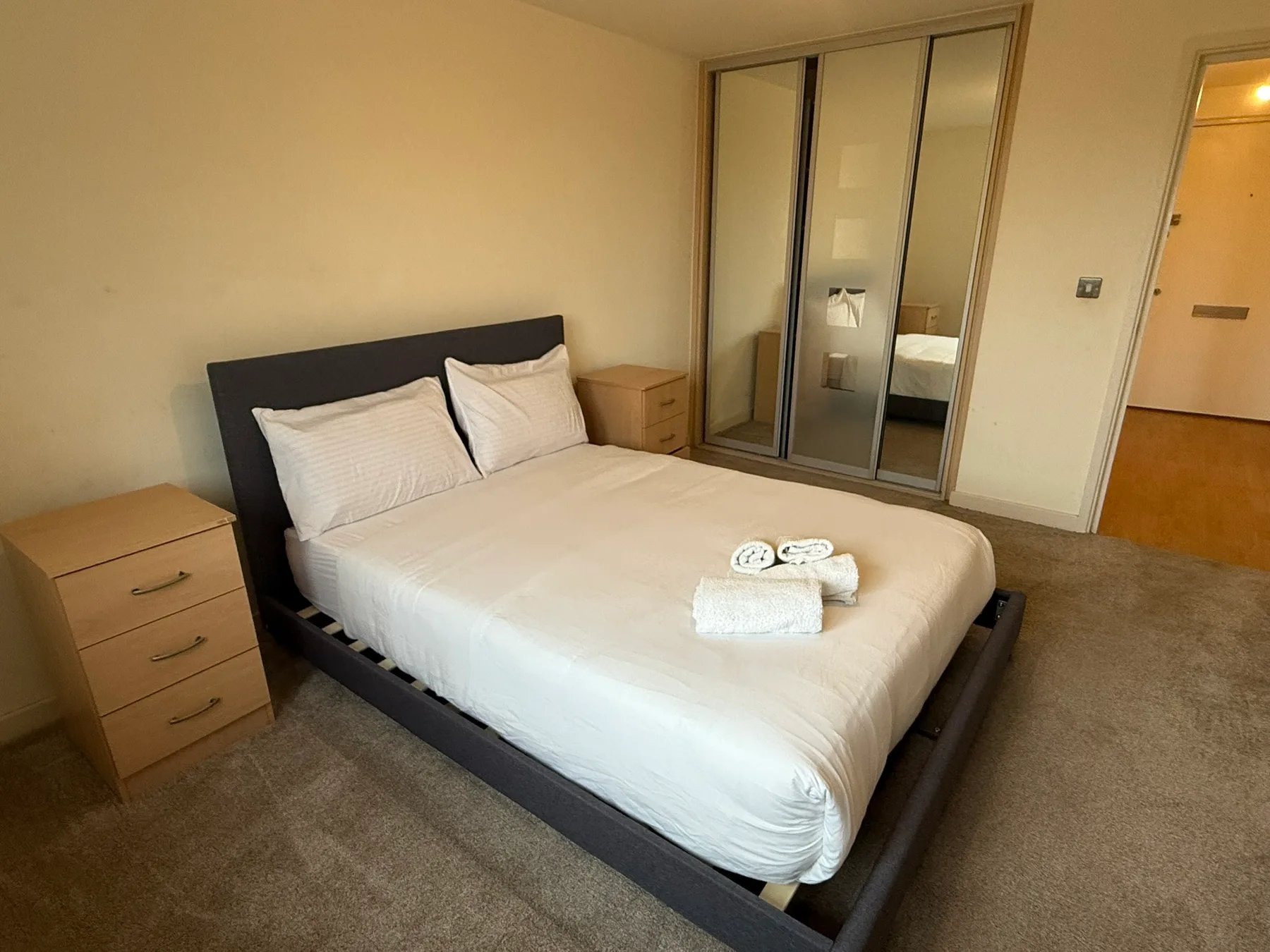 A bedroom with a bed, bedside tables, and mirrored wardrobe doors.