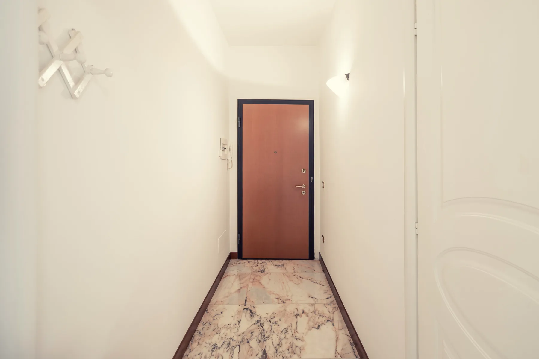 A narrow interior hallway leads to a reddish-brown door, with patterned flooring.