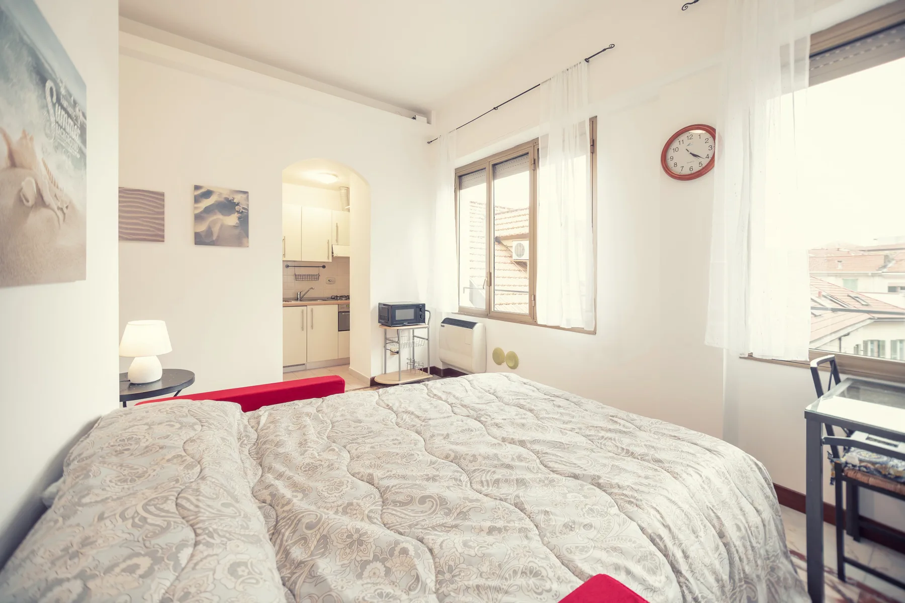 A bright bedroom with a patterned bedspread and large windows.