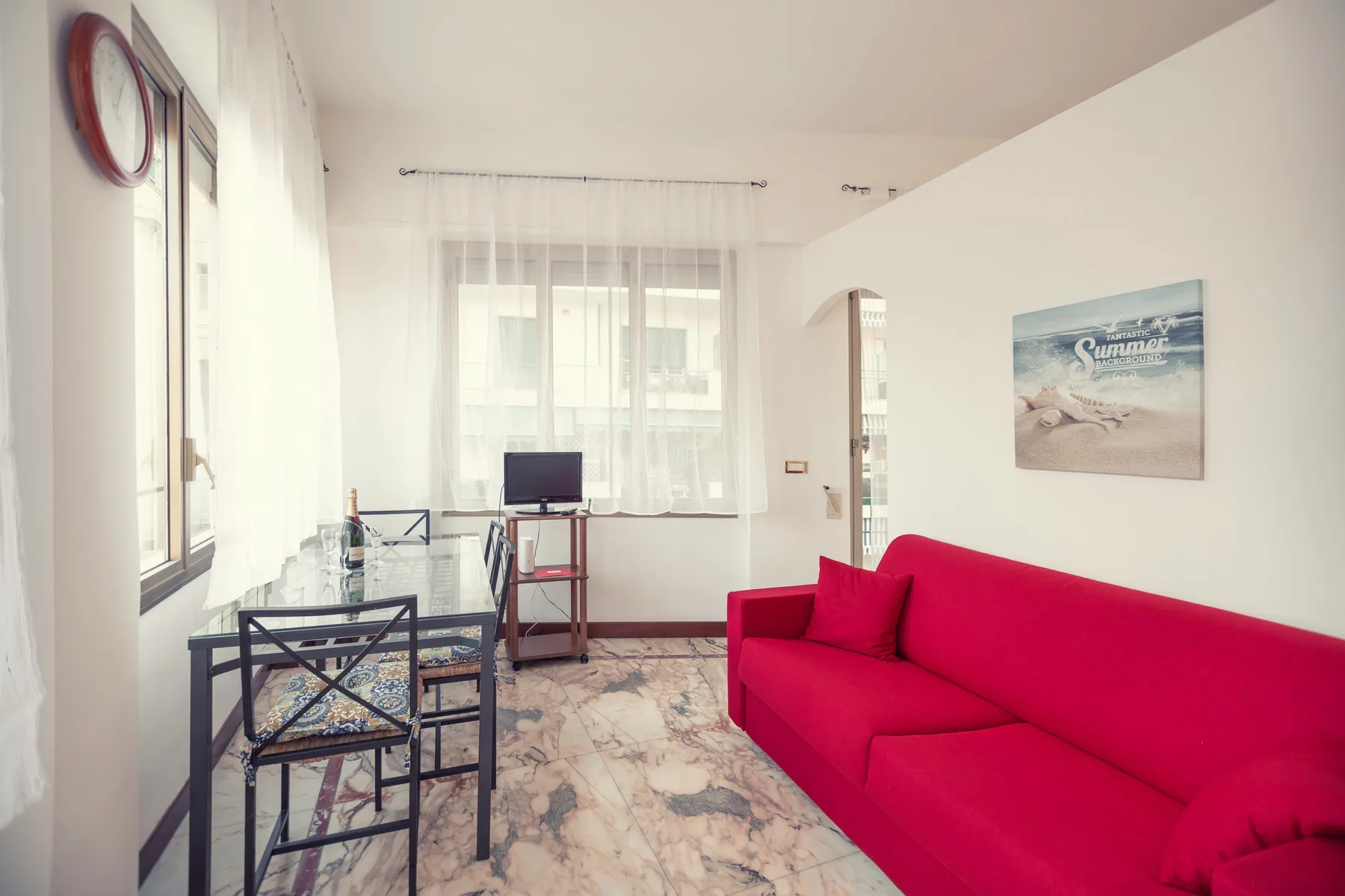 A bright living room with a red sofa, glass coffee table, and television.