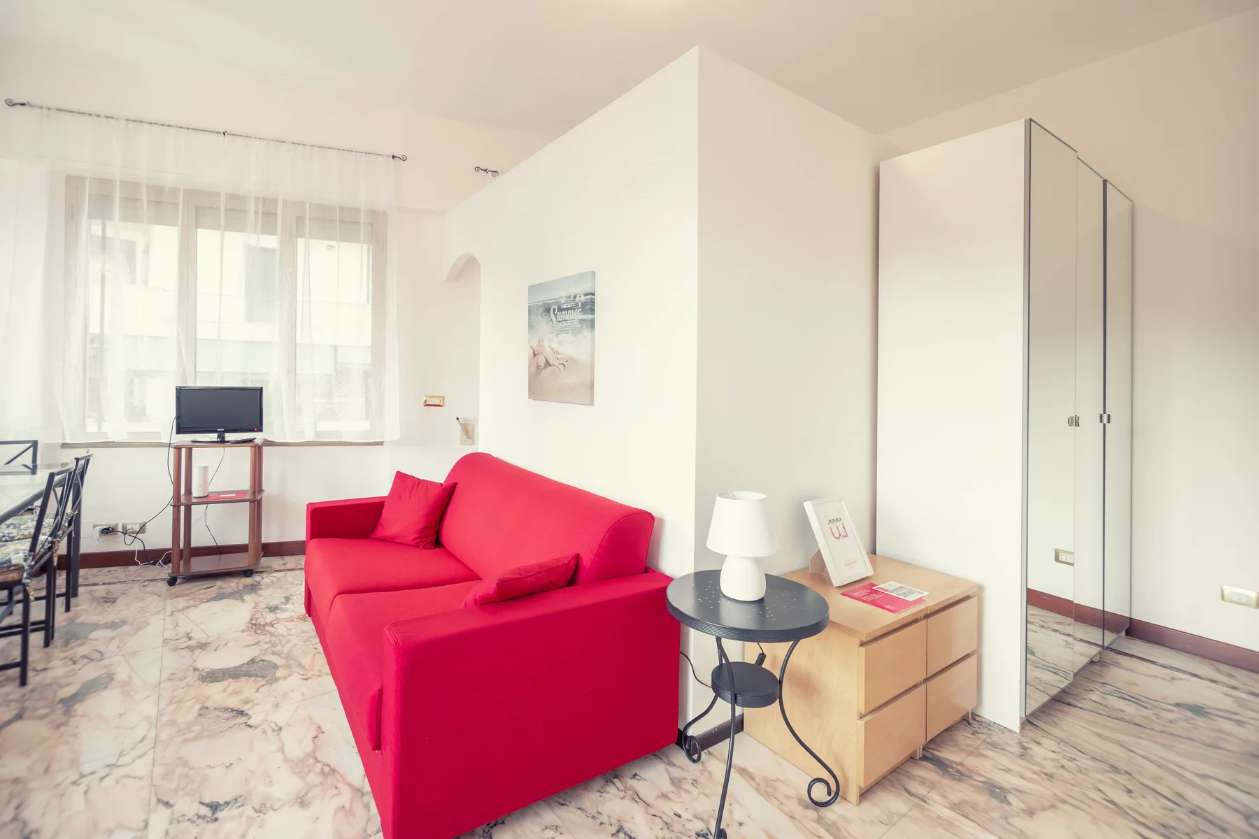 A bright living room with red seating beside a small table and dresser.