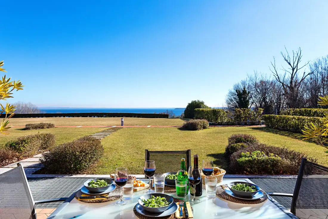 An outdoor dining table overlooks a grassy garden and the sea.