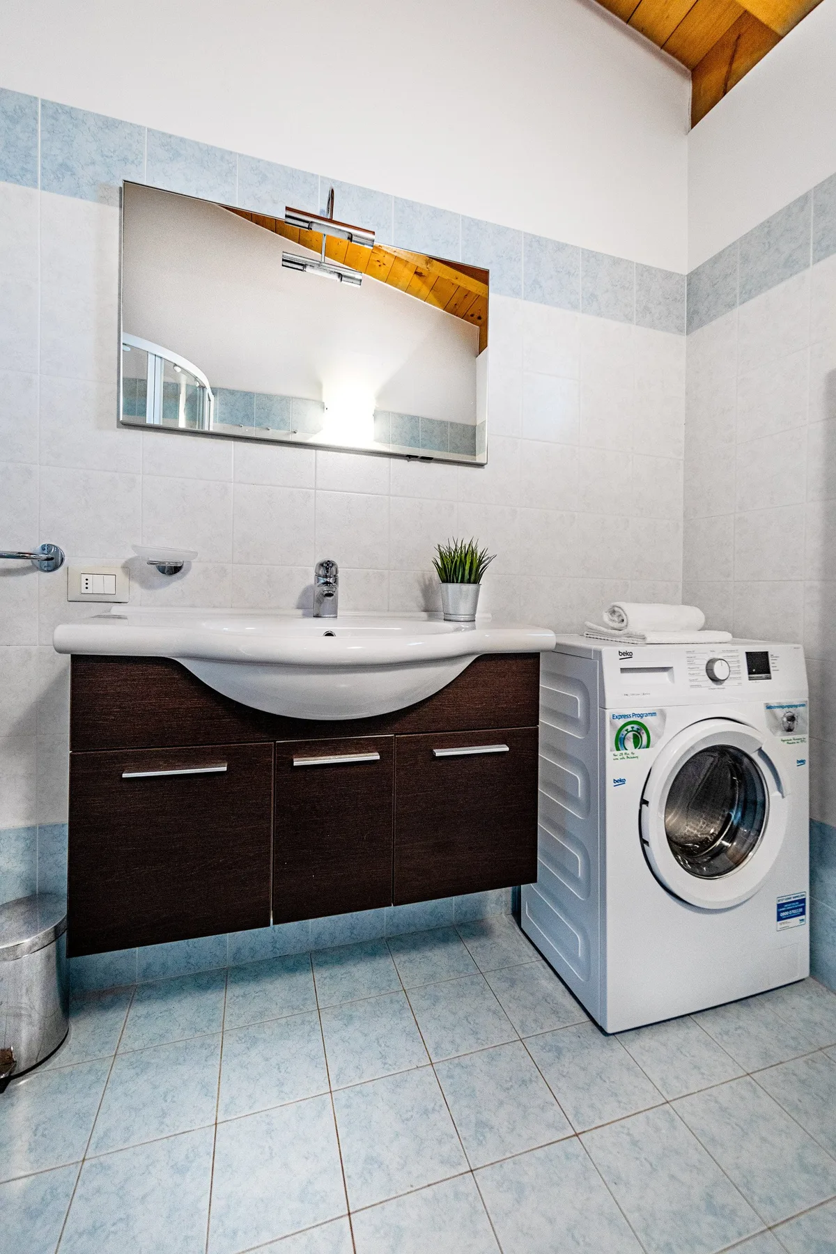 A tiled bathroom with a vanity sink and washing machine beneath a wall mirror.