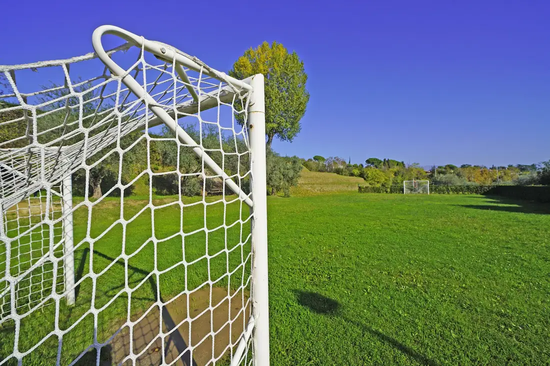 A soccer goal stands beside a broad green field under a clear blue sky.
