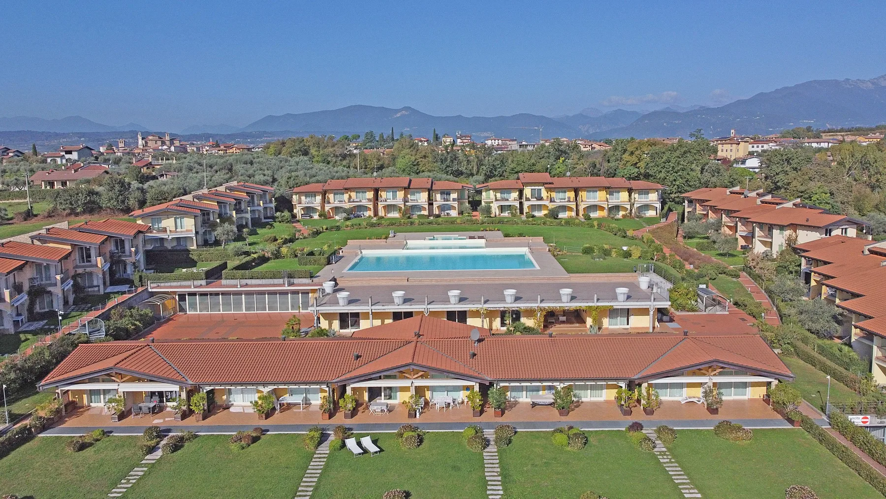 Aerial view of a landscaped resort complex with red-tiled buildings and a swimming pool.