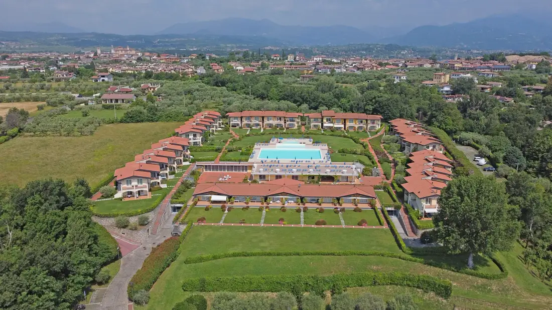 Aerial view of a resort complex with red-roofed buildings surrounding a pool.