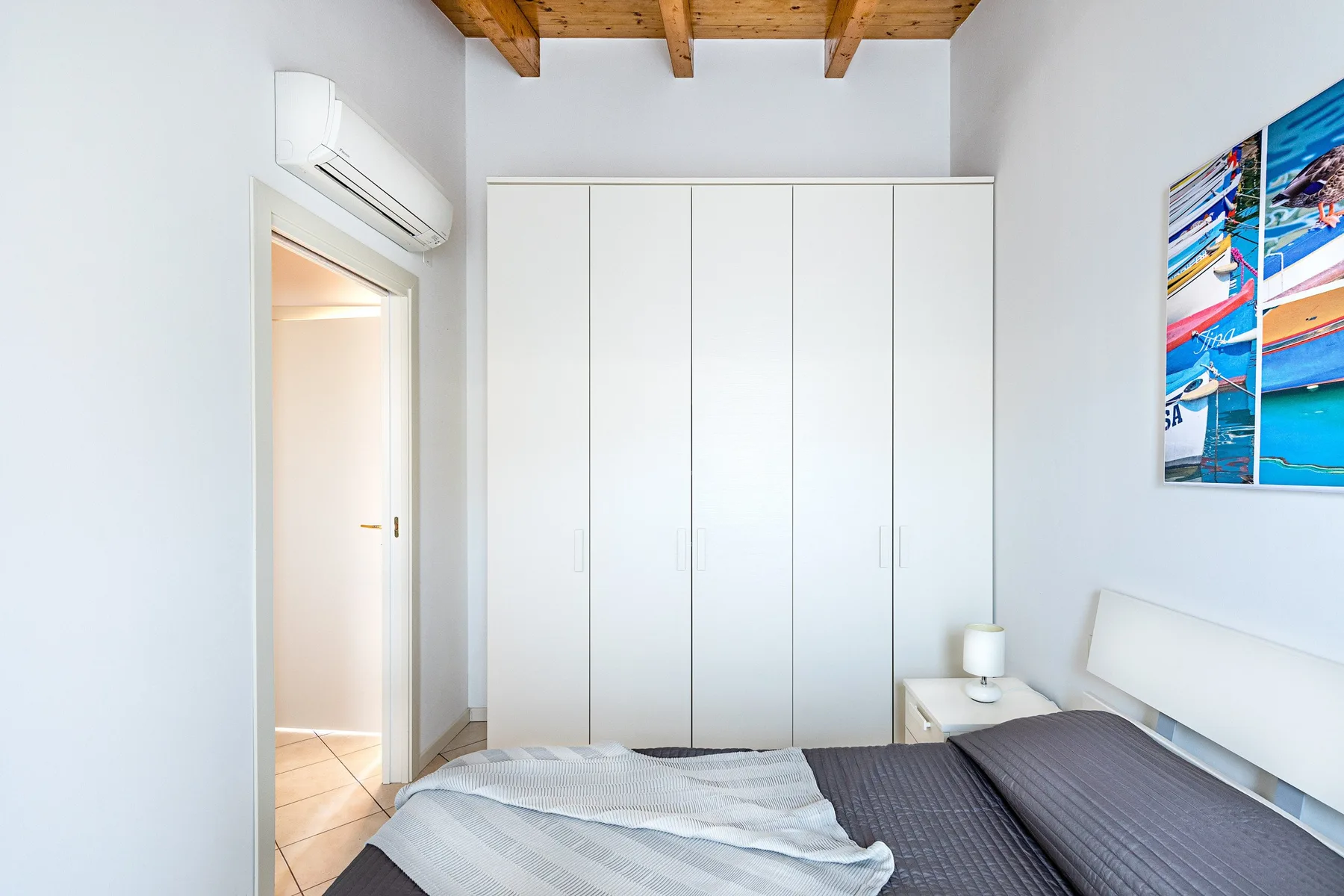 A bedroom with a bed, white wardrobe, and exposed wooden ceiling beams.