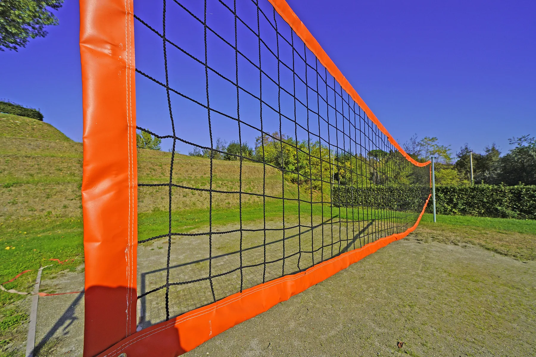 An outdoor sports field with an orange-framed net across the grass.
