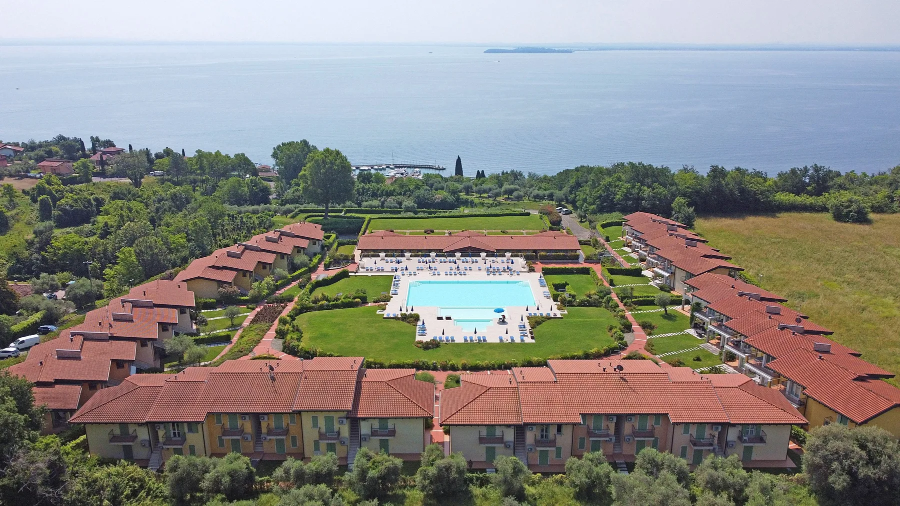 Aerial view of a coastal resort complex with red-roofed buildings and a central pool.
