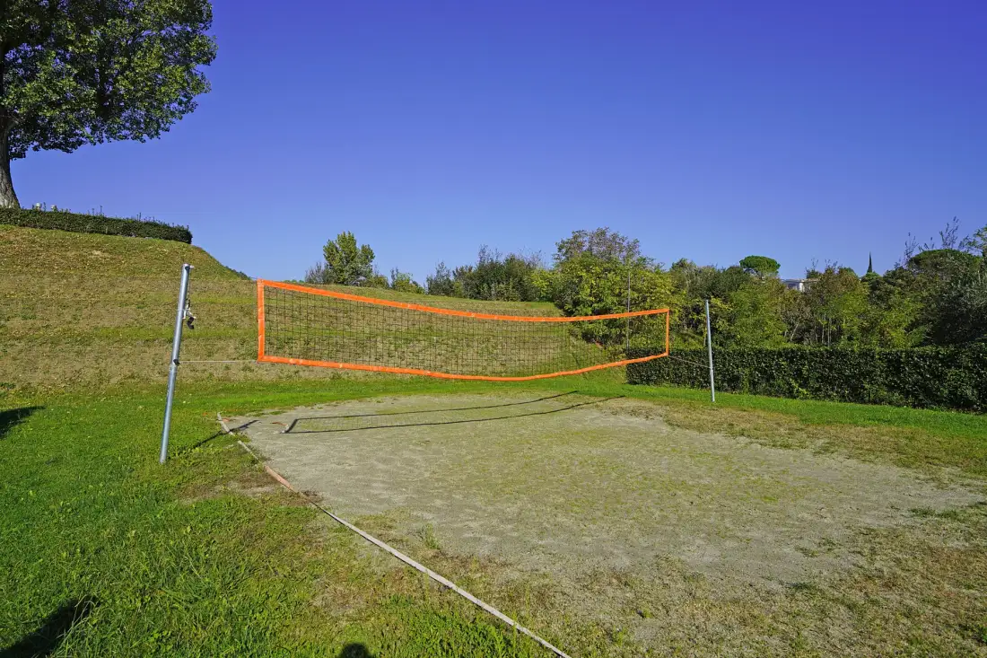 An outdoor volleyball court with an orange net and grassy surroundings.