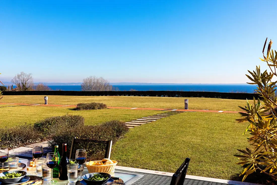 A grassy outdoor dining area overlooks the sea, with a table set in the foreground.