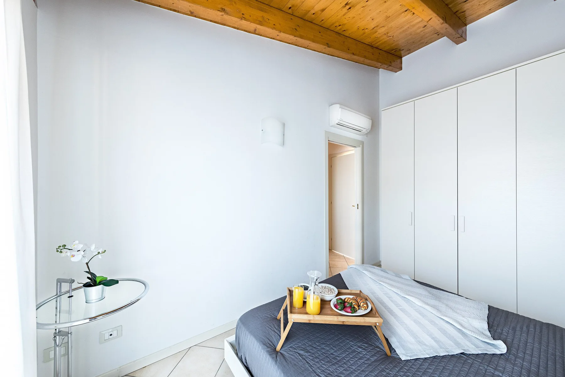 A bedroom with a bed and a wooden tray holding food and drinks.