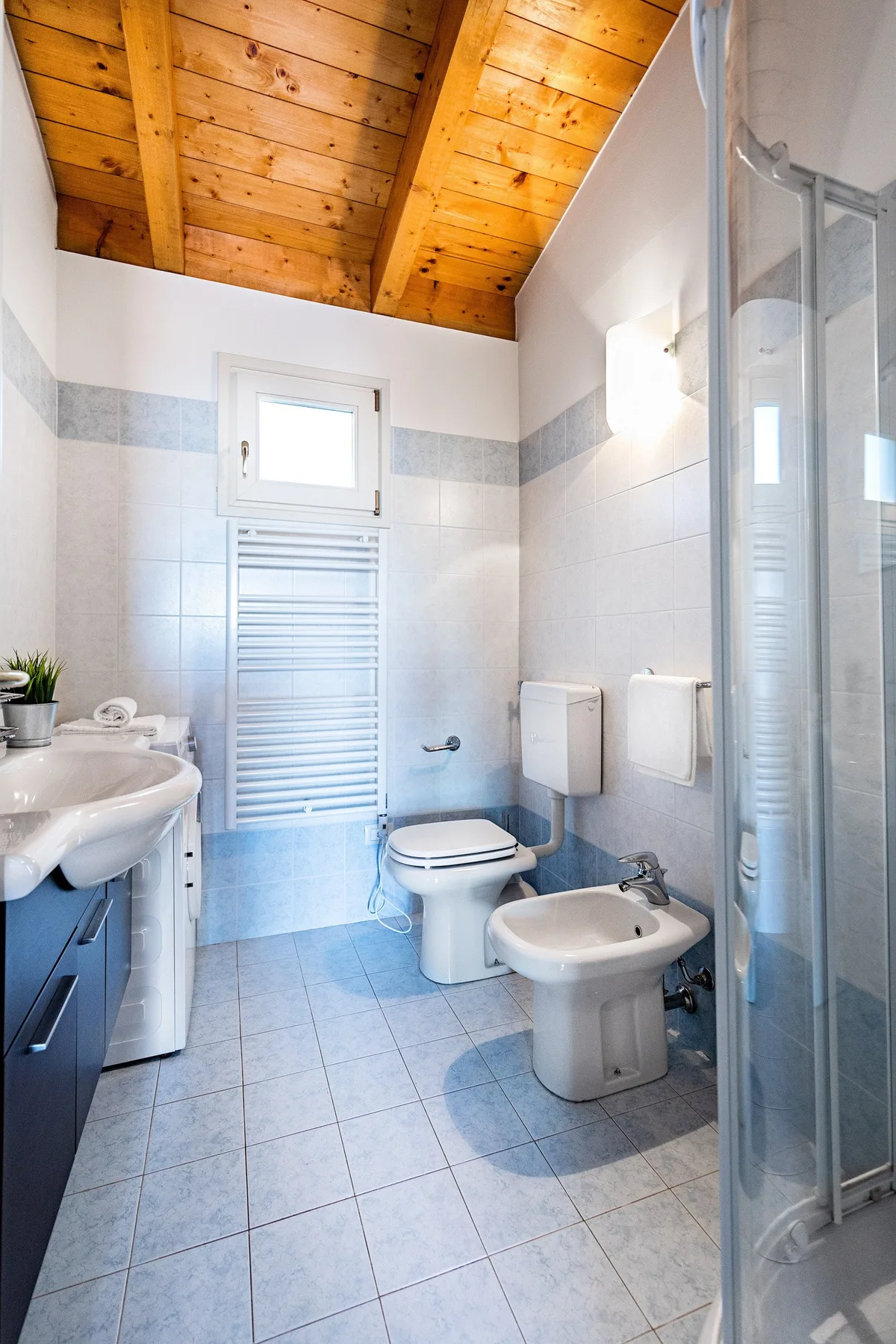 A tiled bathroom with a sink, toilet, bidet, and glass shower enclosure.