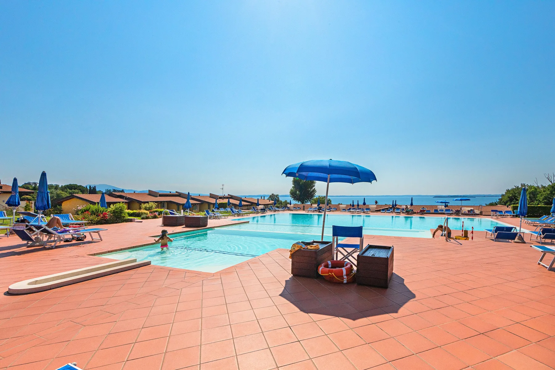 An outdoor swimming pool sits beside a broad tiled deck under a clear sky.