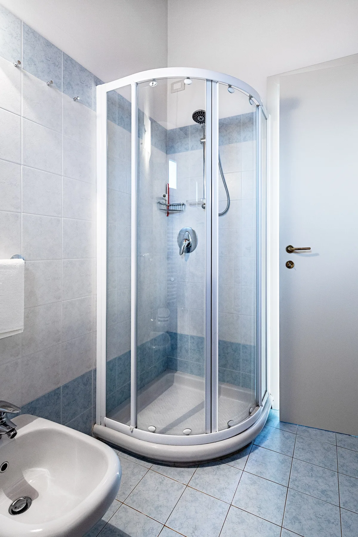 A tiled bathroom with a curved glass shower and a sink.