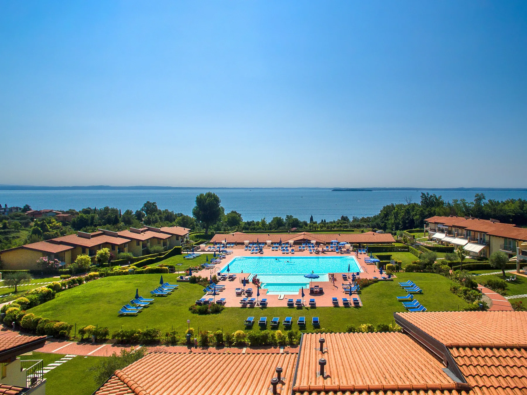 A resort pool area with lounge seating and the sea visible beyond.