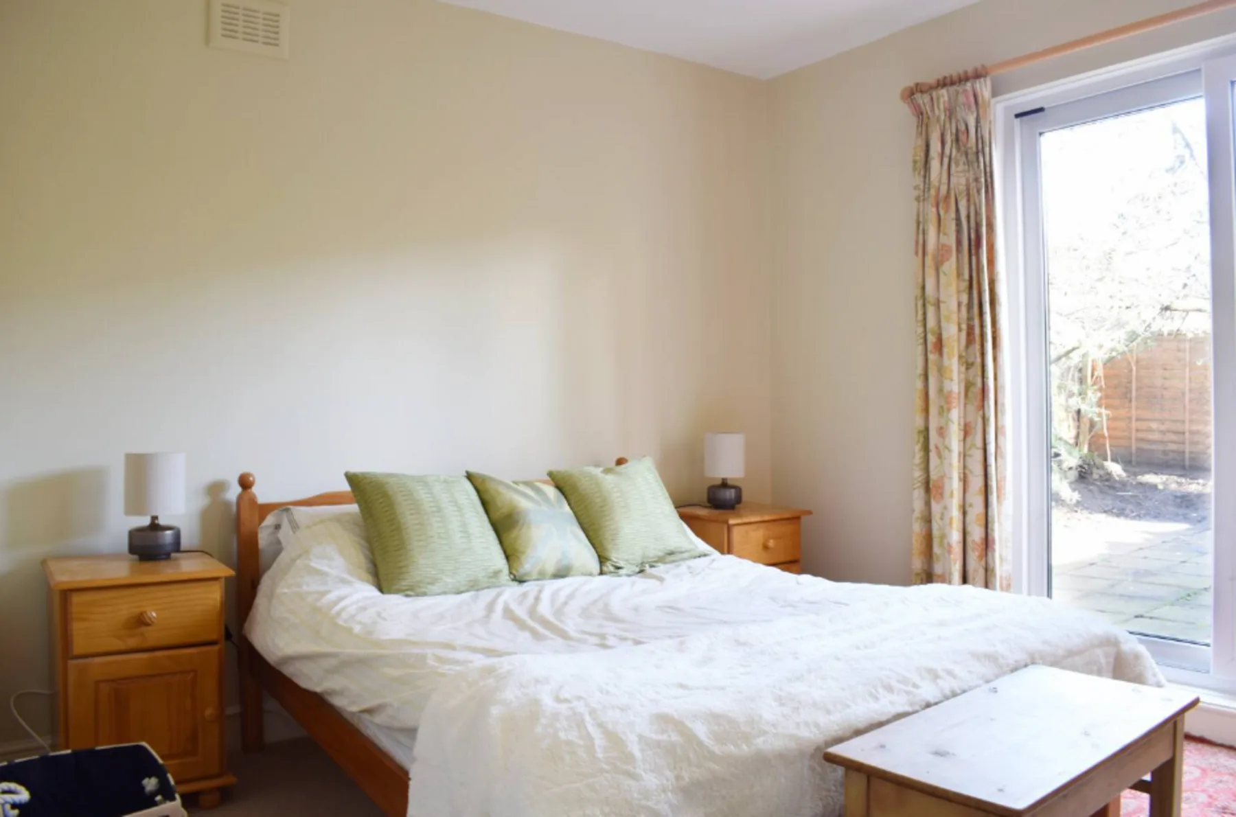 A bedroom with a bed, bedside tables, and a glass door opening onto a patio.