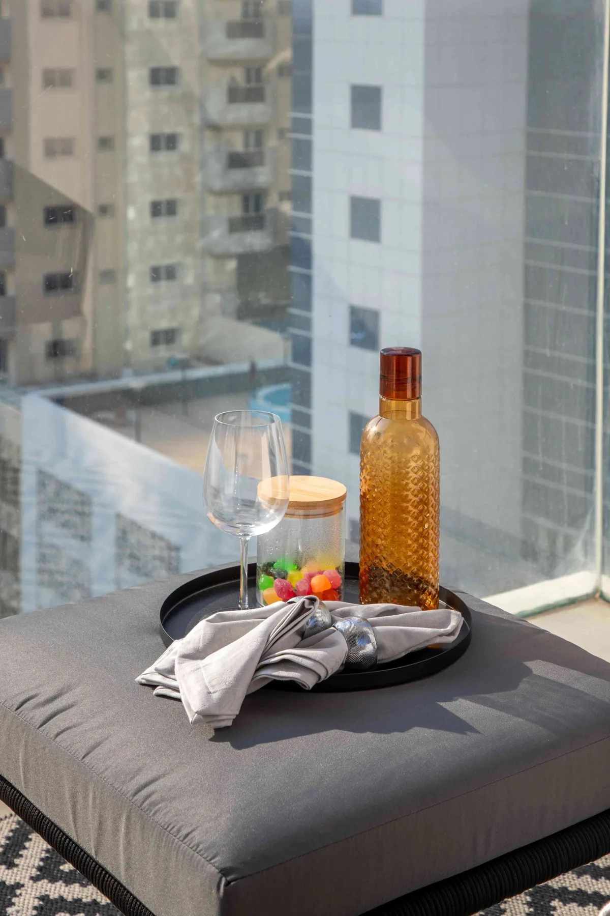 A serving tray with a bottle, glasses, fruit, and folded napkins rests on a cushioned seat by a window.