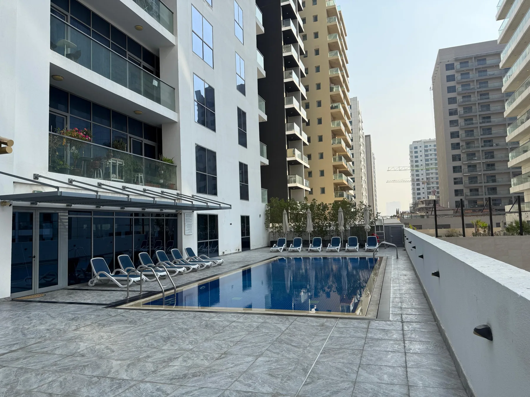A swimming pool and lounge seating sit beside a modern high-rise building.