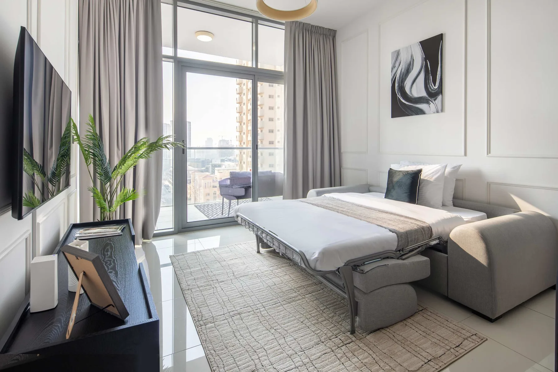A bright bedroom with a bed, bedside seating, and large windows opening onto a balcony.