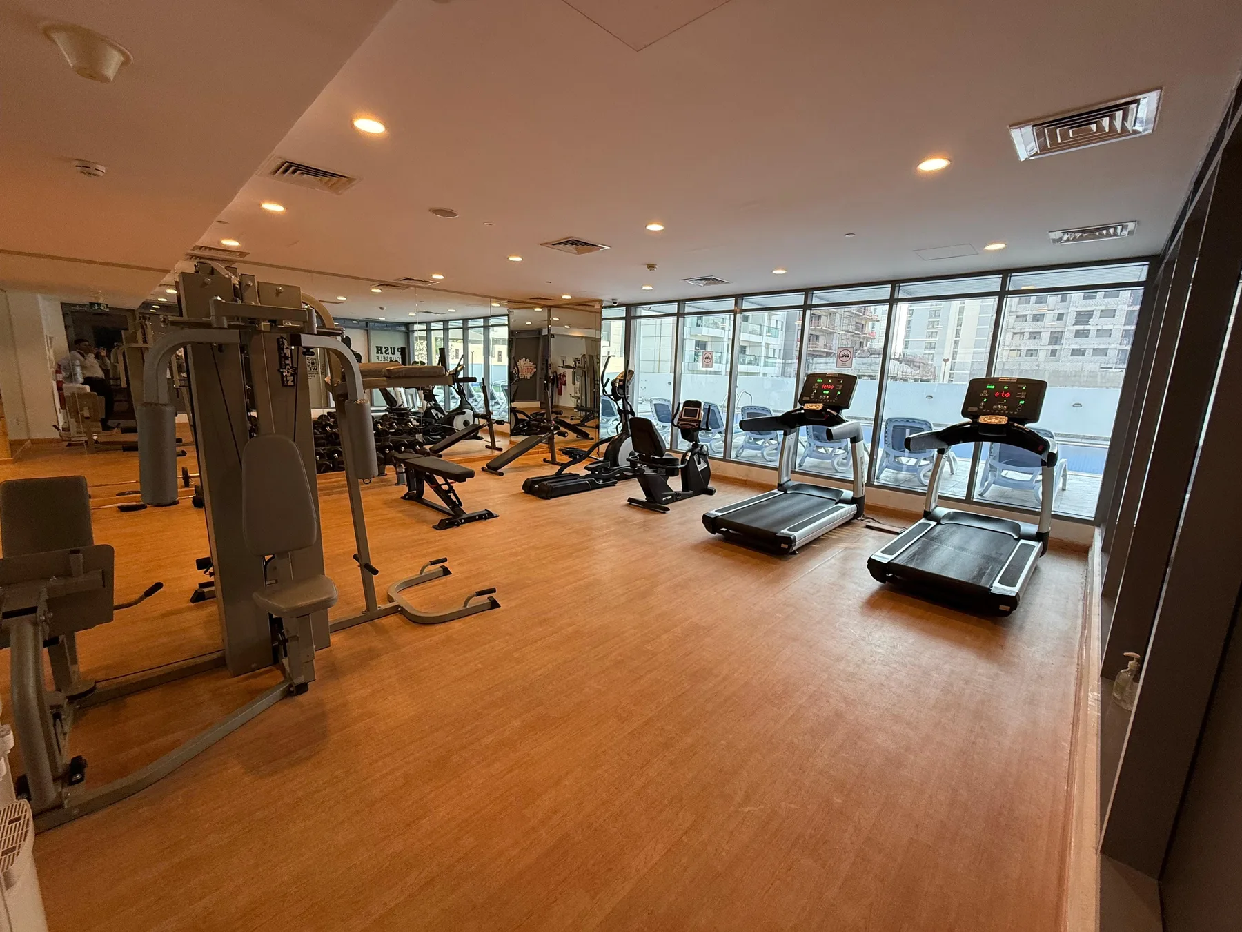 A fitness room with exercise machines and treadmills beside large windows.
