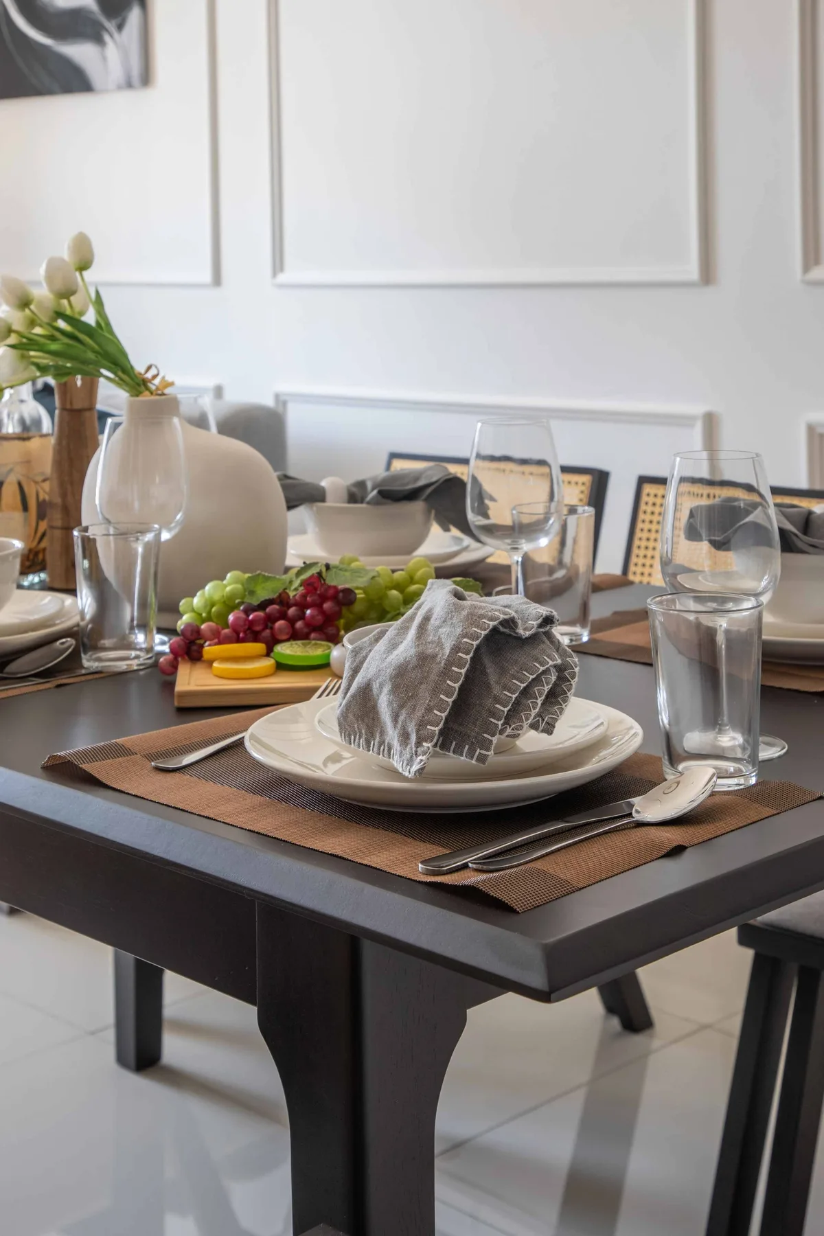 A dining table is set with plates, glasses, and a platter of fruit.