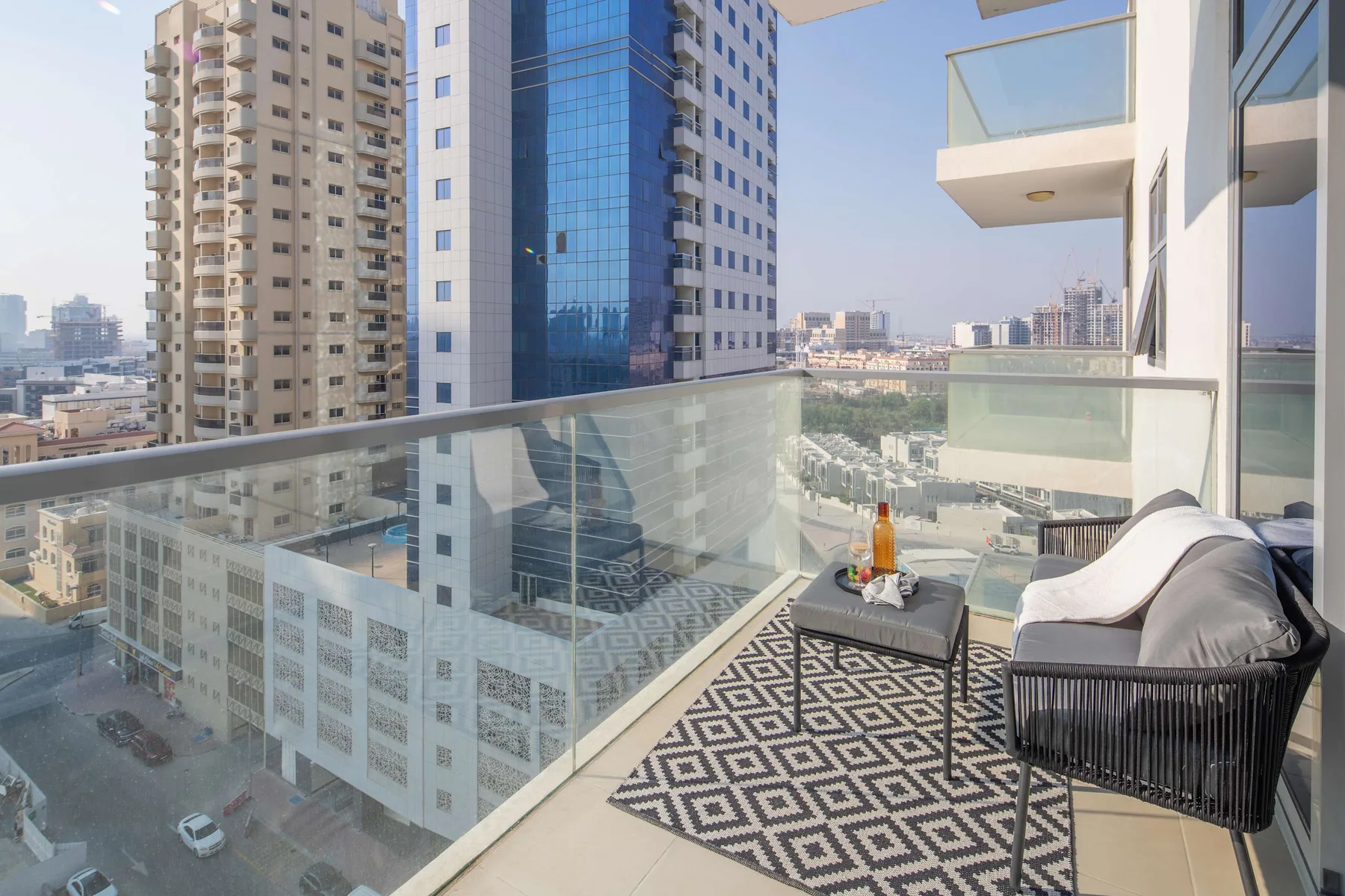 A balcony with glass railings, outdoor seating, and views of nearby city buildings.