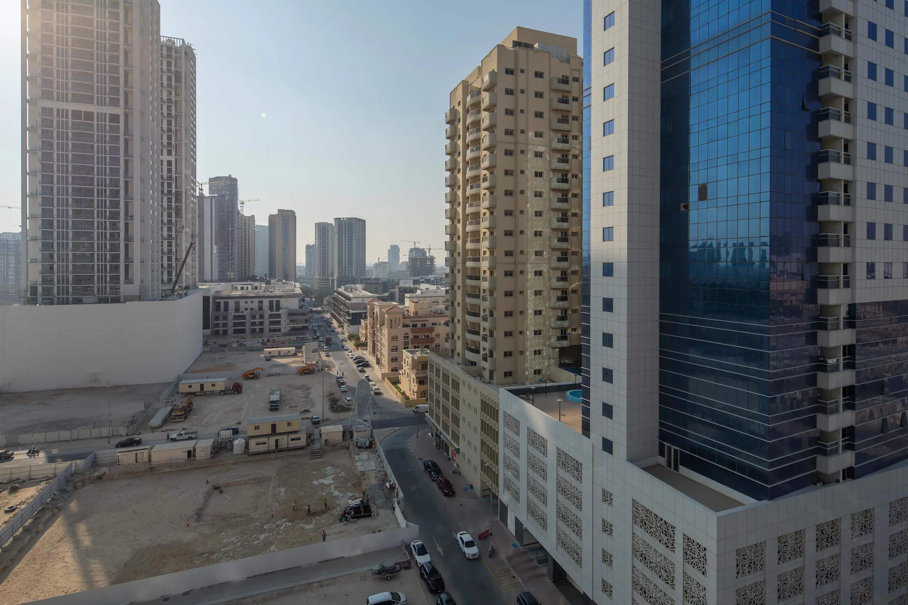 A city street runs between tall buildings, with a construction site in the foreground.