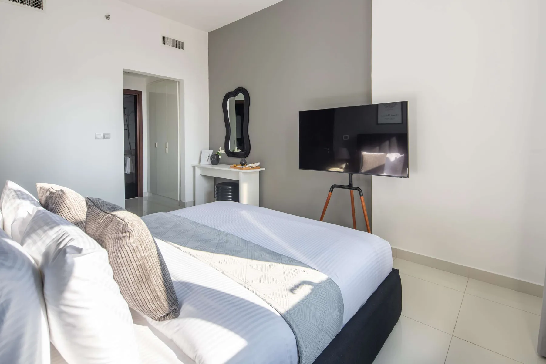 A bright bedroom with a neatly made bed and a wall-mounted television.