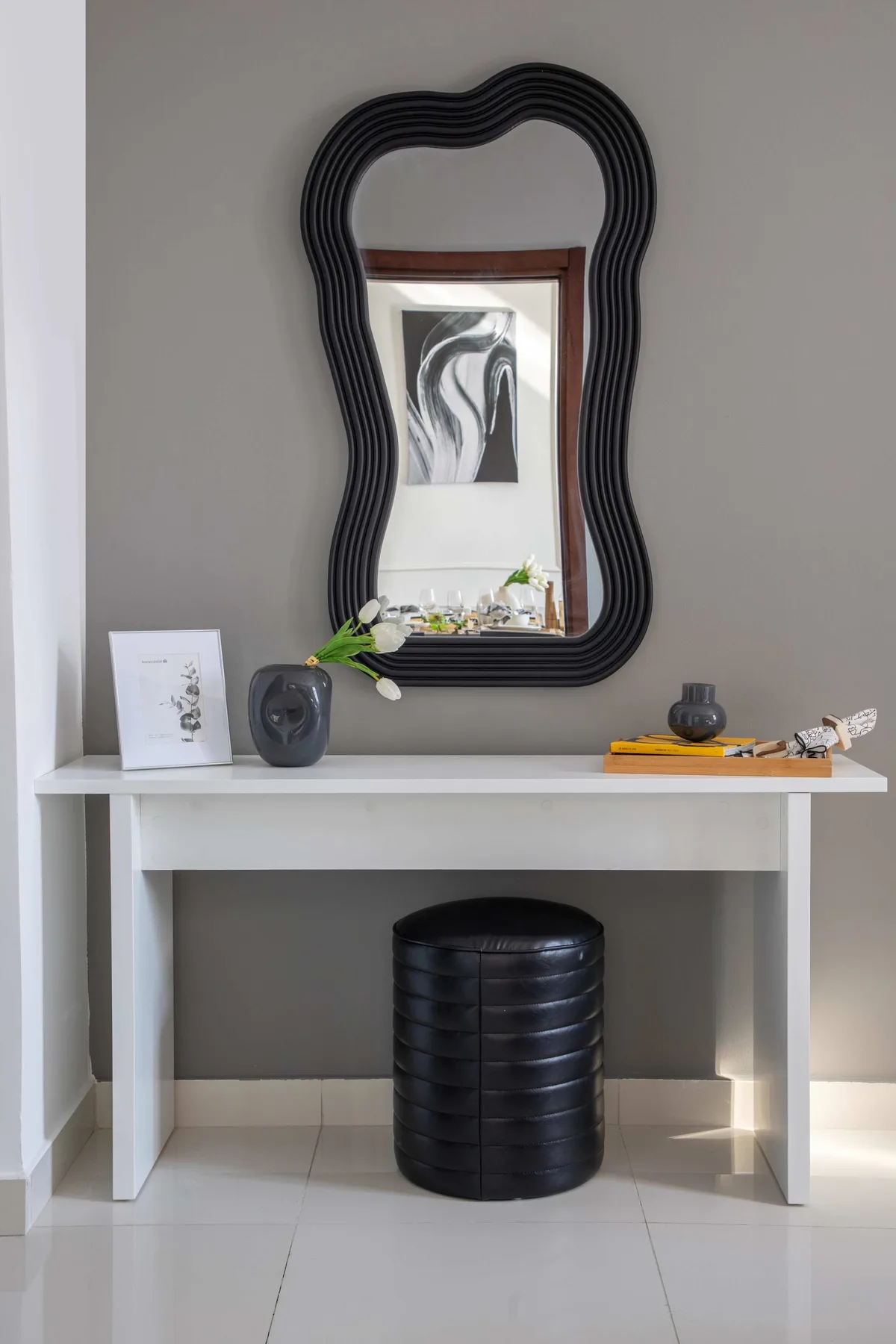 A white console table with a black wavy-edged mirror against a gray wall.