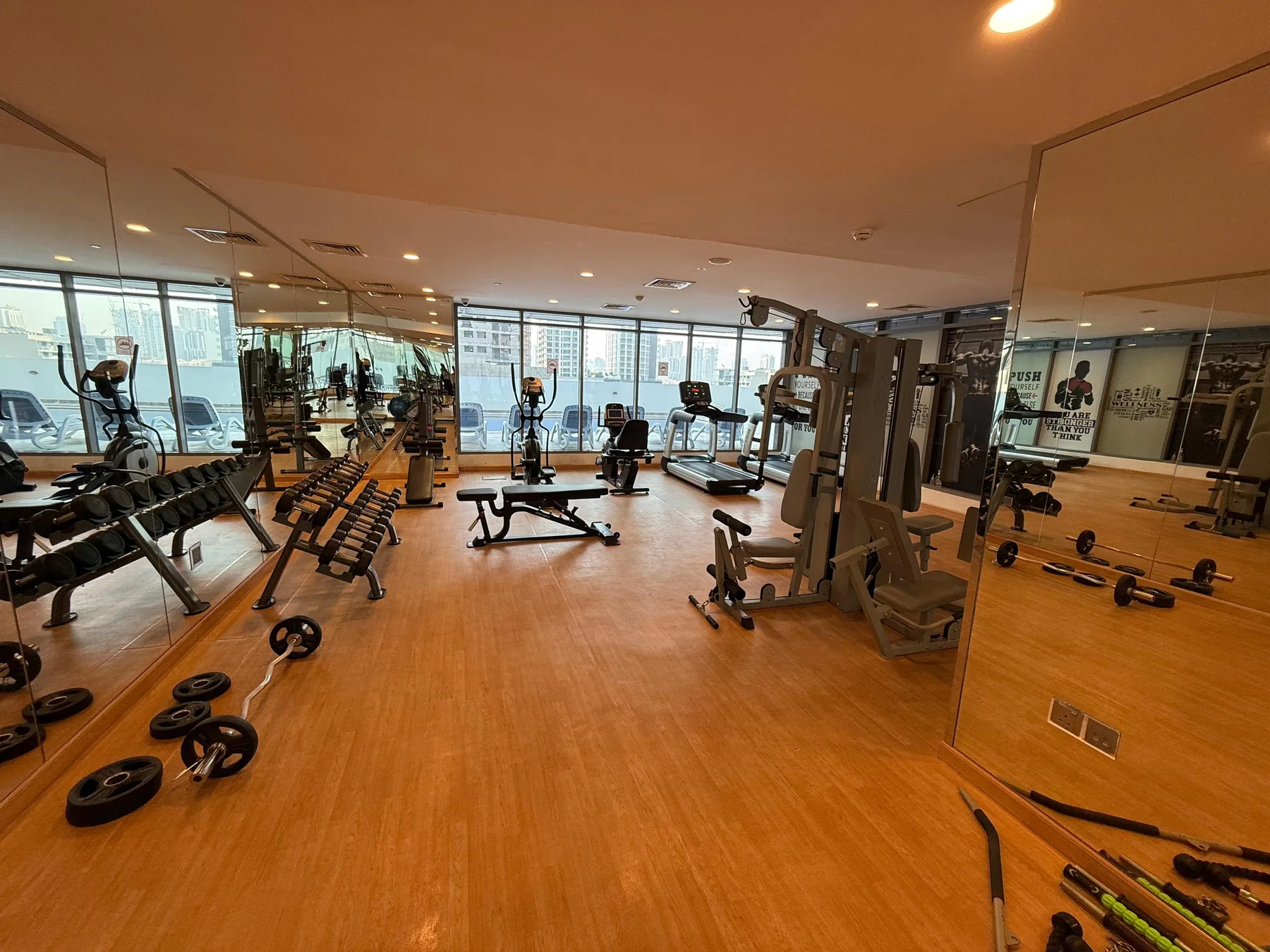 A gym with exercise machines and weights arranged across a wood-toned floor.