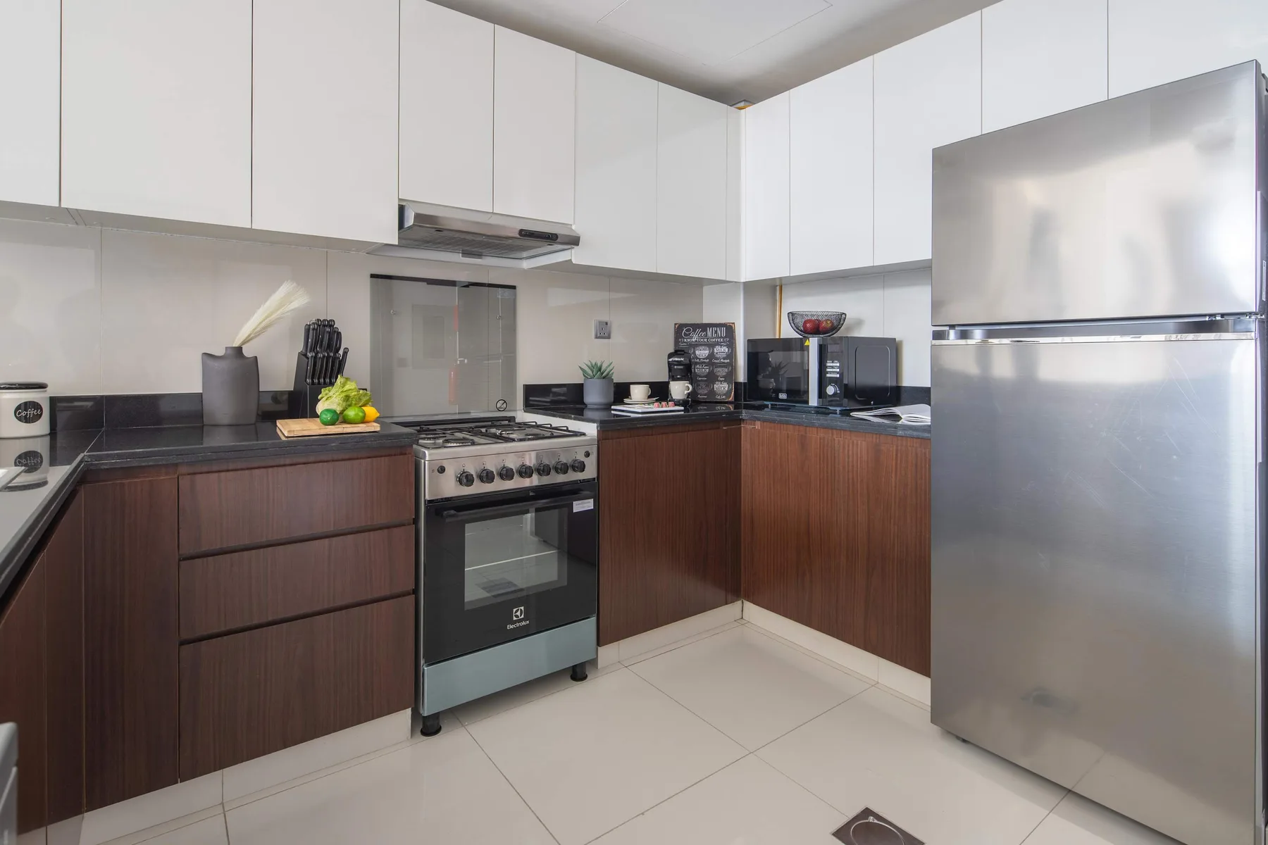 A modern kitchen with dark lower cabinets, white upper cabinets, and stainless steel appliances.