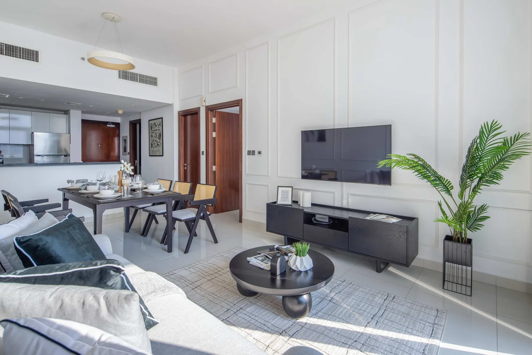 A bright living and dining area with seating, a table, and a wall-mounted television.