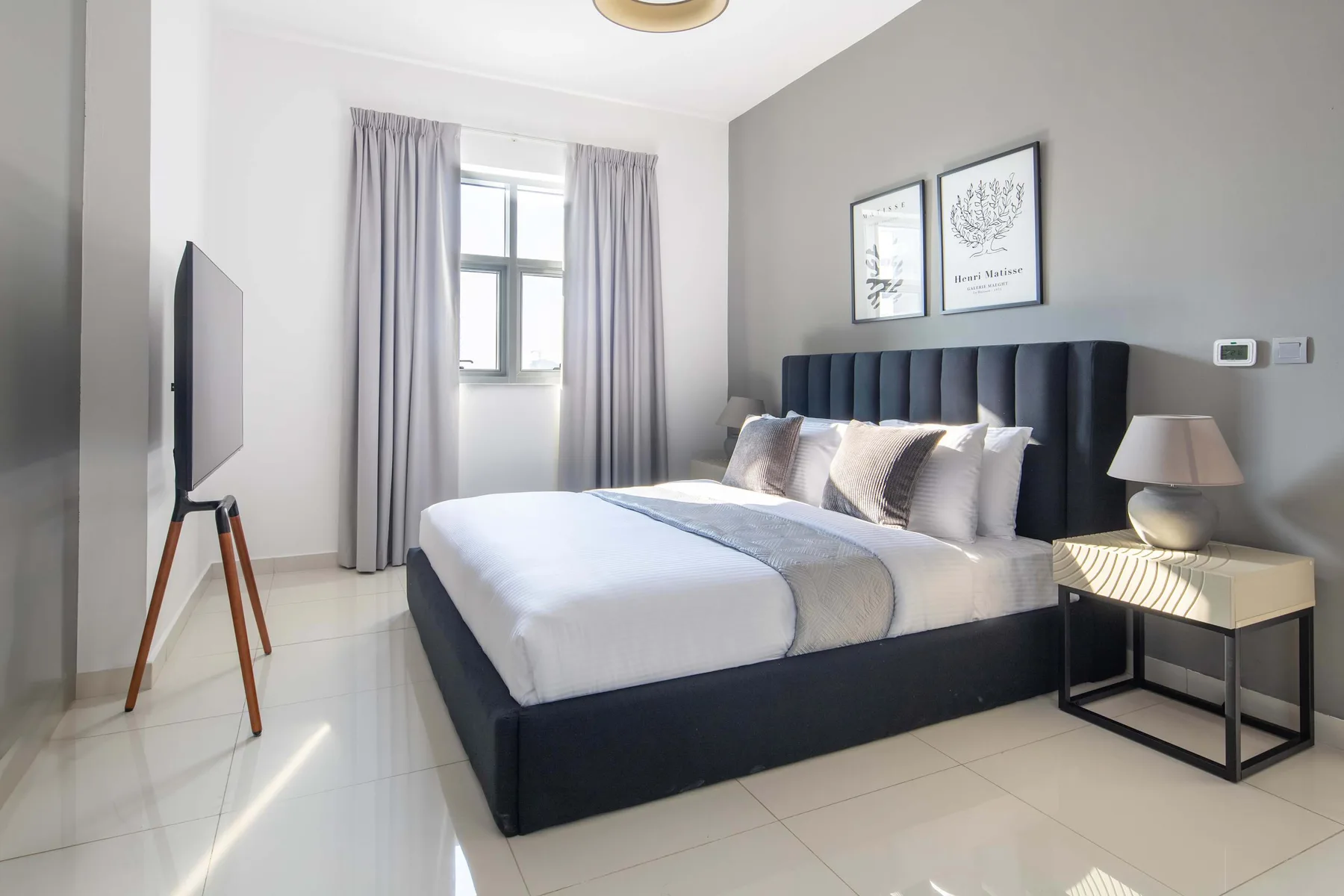 A bedroom with a bed, gray curtains, and framed wall art.