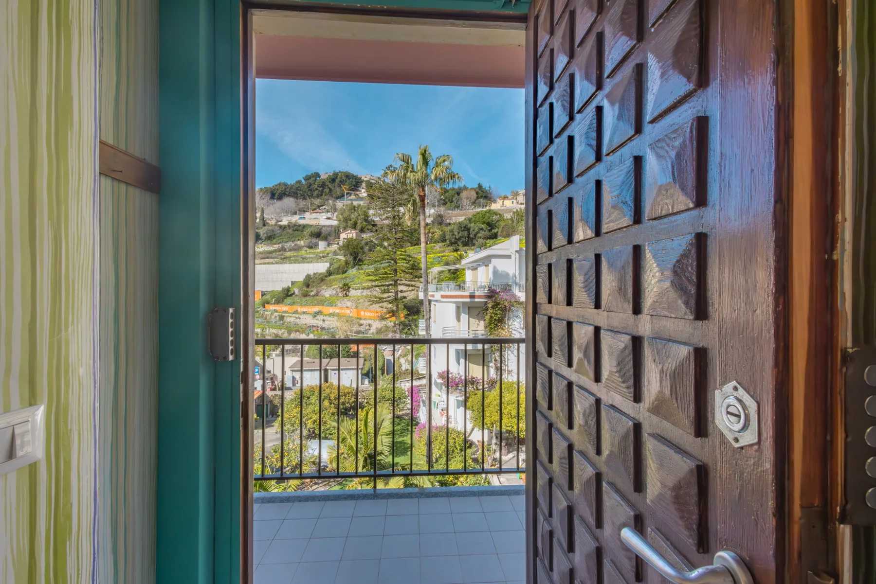 Una puerta abierta da a un balcón con vistas a un barrio en la ladera.