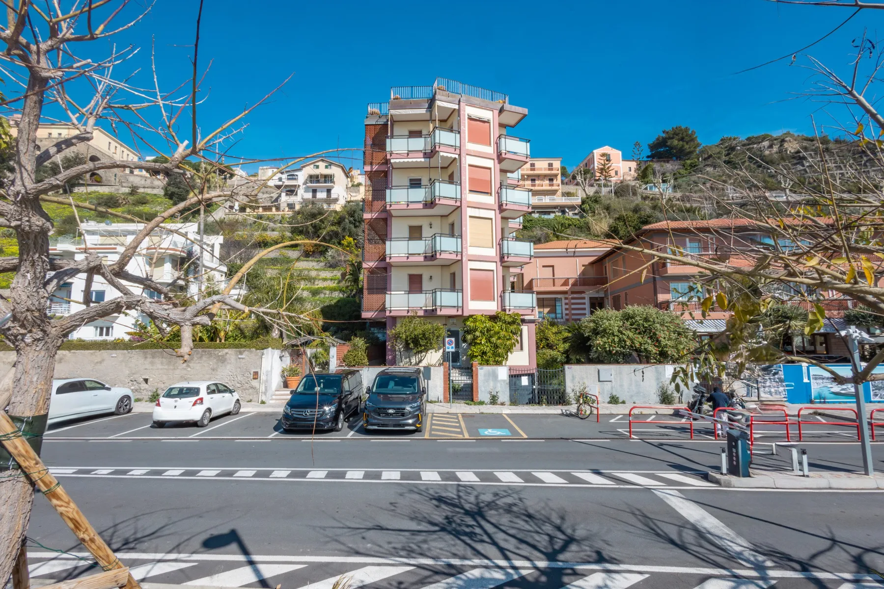 Una calle con un edificio de apartamentos de varias plantas y coches estacionados.
