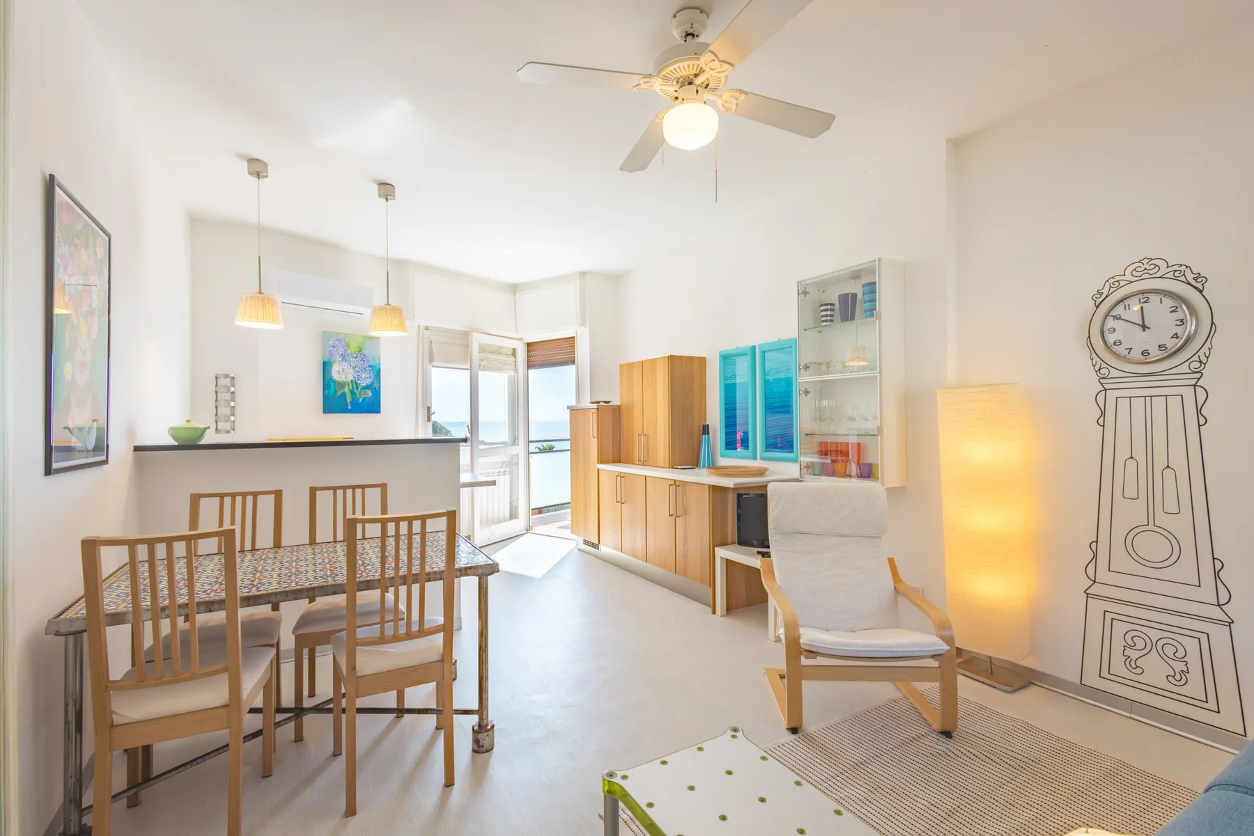 Un luminoso espacio abierto de comedor y sala tiene una mesa, asientos y un ventilador de techo.